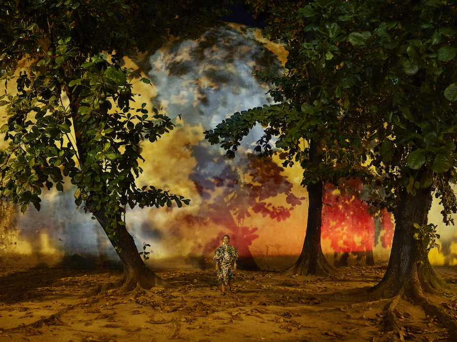 transgender person Luana Muniz amongst trees and colorful backdrop