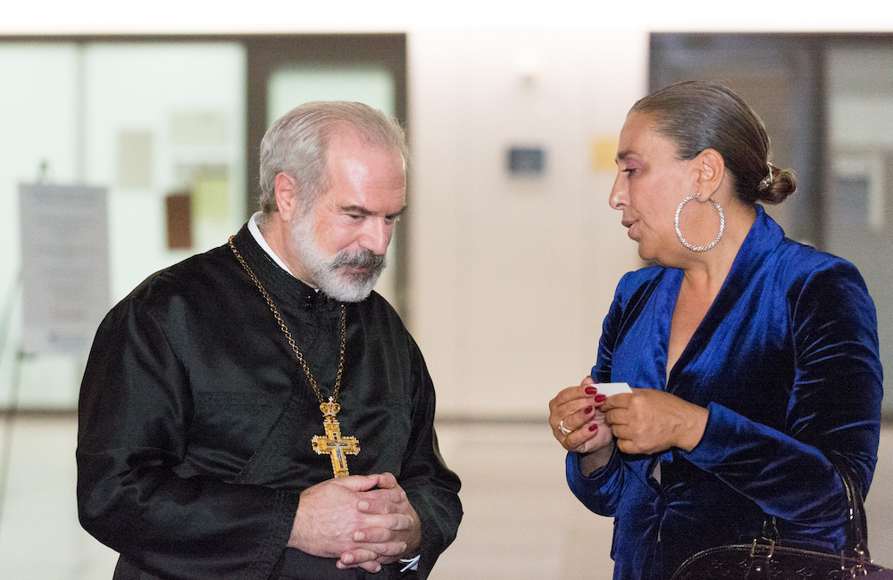 A man in priest attire talking with a woman