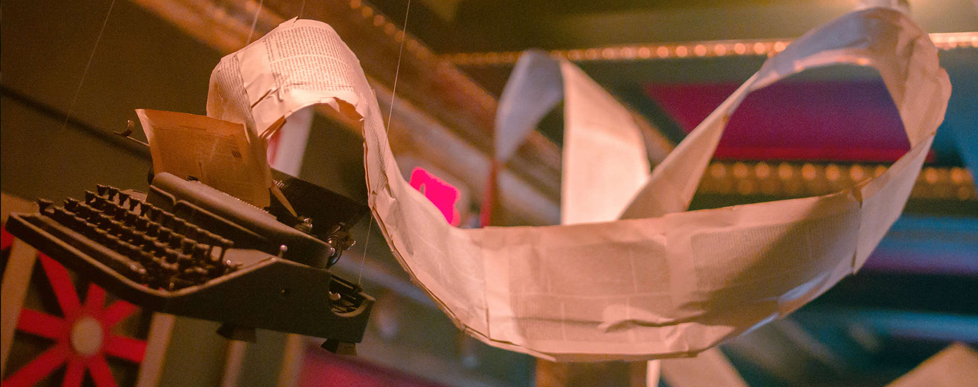 A typewriter suspended from a ceiling with pages flowing out of it