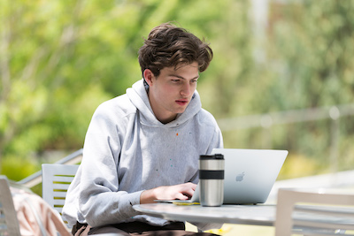 A student working on his laptop outdoors