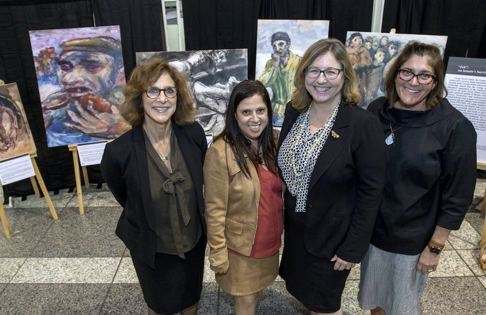 A group of women stand smiling in front of the art exhibition