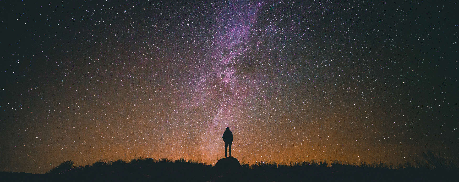 Wide shot of person standing on hill in the dark with stars in the sky