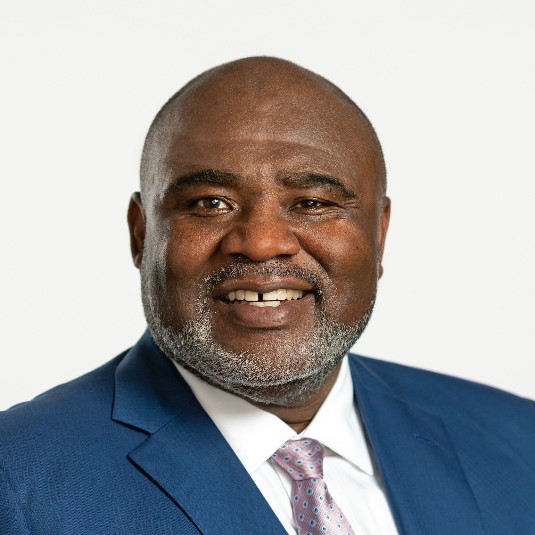 Man wearing blue suit with white shirts and tie against white background and smiling