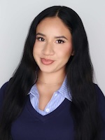 Female with long dark hair wearing blue oxford and navy pullover sweater gray background