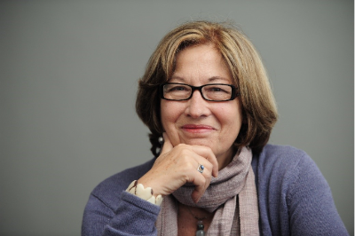 Women with light brown hair glasses hand on chin gray background