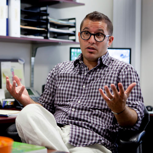 A faculty member sitting in a chair while speaking to someone off screen