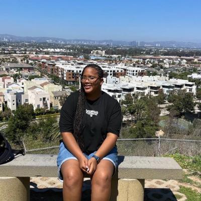 Young woman in black tshirt sitting on bench overlooking bluff and smiling