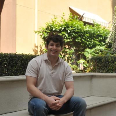 A photo of David Eisman sitting on a stone bench in jeans and a gray short-sleeved collared shirt